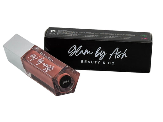 This image features a product named "Strike," presented by the brand "Glam by Ash Beauty & Co." The product is displayed alongside its packaging, which is elegantly designed in black with the brand name prominently displayed.